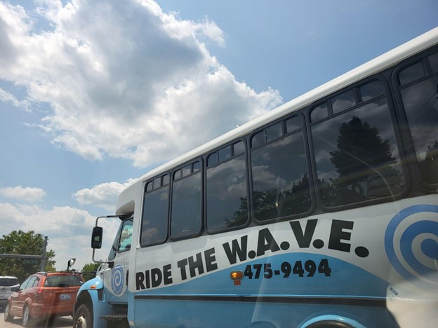 A WAVE bus sits in traffic. Ride the WAVE is emblazoned along the side.